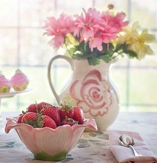 bowl of strawberries with pitcher of flowers behind
